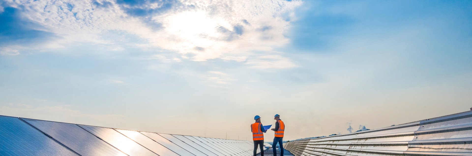 Two men on roof with solar panels, both wearing PPE