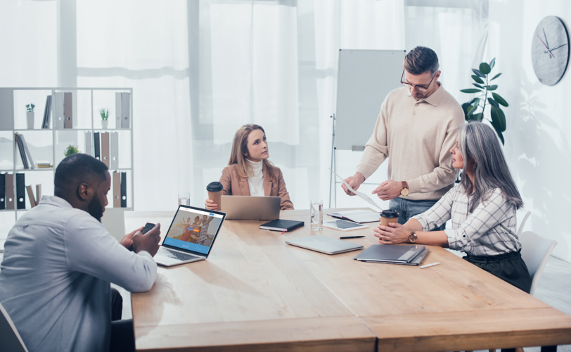 Team meeting, four people in a meeting room with laptops and documents