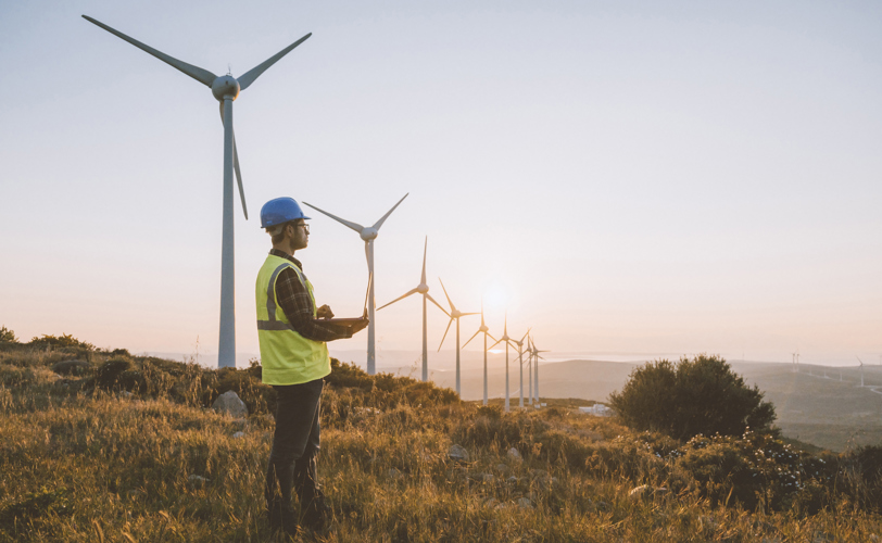 Man stood near windmills, on a hilltop wearing PPE and holding a clipboard